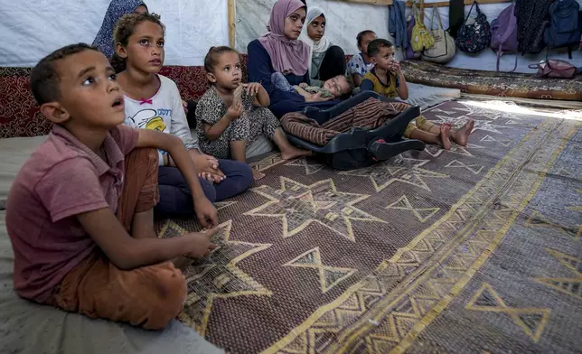 CAPTION CORRECTION: Displaced infant Abdel-Rahman Abu El-Jedian, 11-month-old, who suffers from polio, is carried by his mother, center, at a makeshift tent camp in Deir al-Balah, central Gaza Strip, Tuesday, Aug. 27, 2024. (AP Photo/Abdel Kareem Hana)