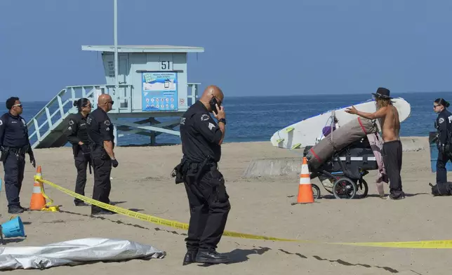 Tyler Eyre, 30, from Salt Lake City, Utah, tries to salvage a few extra possessions as police and Los Angeles County Department of Beaches and Harbors workers cordon off his beach camp during a cleanup operation to remove homeless encampments at the Dockweiler State Beach in Playa del Rey, Los Angeles, on Thursday, Aug. 22, 2024. (AP Photo/Damian Dovarganes)