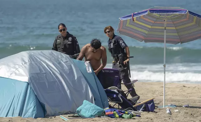 Los Angeles Police demand a man to clean and pack up personal belongings as they conduct a cleanup operation to remove homeless encampments at Dockweiler State Beach in Playa del Rey, Los Angeles, on Thursday, Aug. 22, 2024. (AP Photo/Damian Dovarganes)