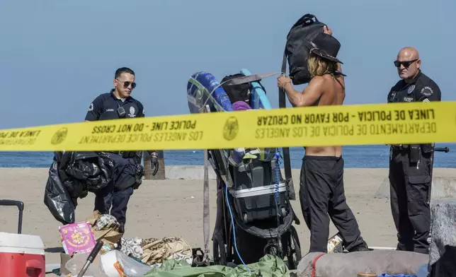 Tyler Eyre, 30, from Salt Lake City, Utah, packs his possessions as police and Los Angeles County Department of Beaches and Harbors workers cordon off his beach camp during a cleanup operation to remove homeless encampments at the Dockweiler State Beach in Playa del Rey, Los Angeles, on Thursday, Aug. 22, 2024. (AP Photo/Damian Dovarganes)