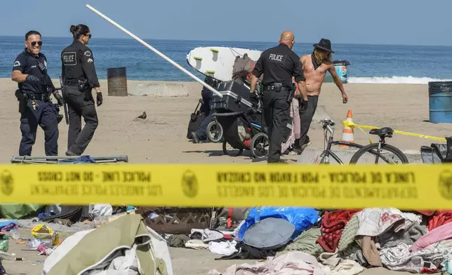 Tyler Eyre, 30, from Salt Lake City, Utah, salvages a few possessions as police and Los Angeles County Department of Beaches and Harbors workers cordon off his beach camp during a cleanup operation to remove homeless encampments at the Dockweiler State Beach in Playa del Rey, Los Angeles, on Thursday, Aug. 22, 2024. (AP Photo/Damian Dovarganes)