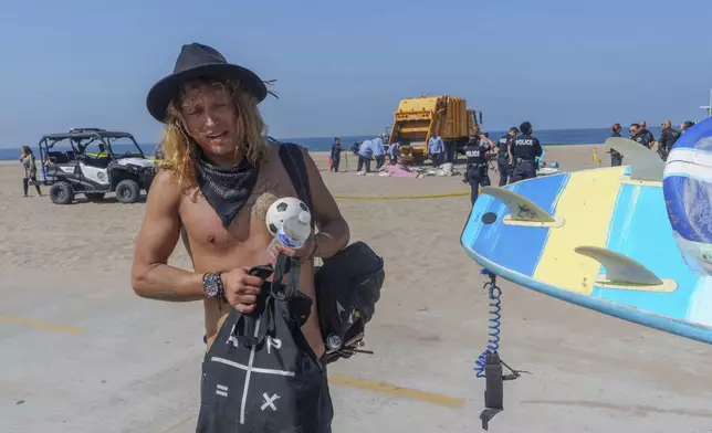 Tyler Eyre, 30, from Salt Lake City, Utah, salvages a few possessions as and beach workers remove his beach camp during a cleanup operation to remove homeless encampments at Dockweiler State Beach in Playa del Rey, Los Angeles, on Thursday, Aug. 22, 2024. (AP Photo/Damian Dovarganes)