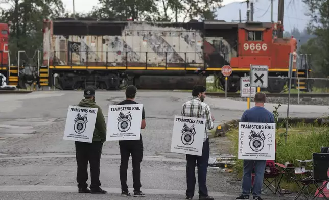 Locked out Canadian National Rail workers stand at a picket line as locomotives are moved by management at CN Rail's Thornton Yard in Surrey, British Columbia, Canada, Thursday, Aug. 22, 2024. (Darryl Dyck/The Canadian Press via AP)