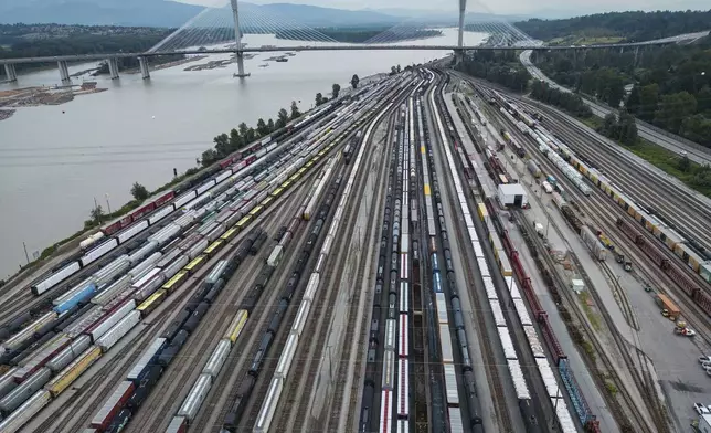 Train cars are seen on the tracks in an aerial view at Canadian National Rail's Thornton Yard as the Port Mann Bridge spans the Fraser River and trucks transport cargo containers on the highway in Surrey, British Columbia, Canada, Thursday, Aug. 22, 2024. (Darryl Dyck/The Canadian Press via AP)