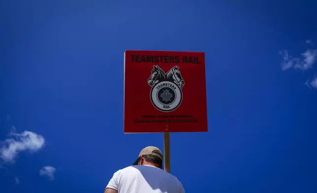 A picketer carries a Teamsters Rail placard at a Canadian Pacific Kansas City (CPKC) rail yard in Smiths Falls, Ontario, Canada, Thursday, Aug. 22, 2024, (Sean Kilpatrick/The Canadian Press via AP)