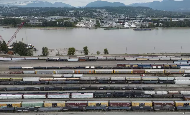 Train cars are seen on the tracks in an aerial view at Canadian National Rail's Thornton Yard as the Port Mann Bridge spans the Fraser River and trucks transport cargo containers on the highway in Surrey, British Columbia, Canada, Thursday, Aug. 22, 2024. (Darryl Dyck/The Canadian Press via AP)