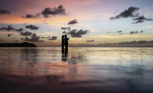 FILE - Tourists watch the sun set along a popular beach in Tamuning, Guam, May 6, 2019. (AP Photo/David Goldman, File)