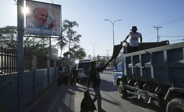 Workers clean up a street near a poster welcoming Pope Francis, in Dili, East Timor, Monday, Aug. 12, 2024. (AP Photo/Achmad Ibrahim)