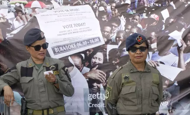 East Timorese police officers stand guard near a banner depicting people queuing up to give their votes in the 1999 referendum, during the commemoration of the 25th year anniversary of the vote for the country's independence from Indonesia in Dili, East Timor, Friday, Aug. 30, 2024. (AP Photo/Carlos Caro Junior)