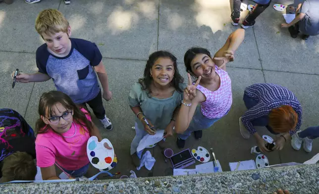 This photo provided by Spokane Public Schools shows Adams Elementary fifth graders pausing to pose for a photo while painting a mural at Spokane Community College, May 2024, in Spokane, Wash. (Spokane Public Schools via AP)