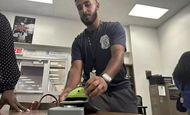 Lackawanna Police Officer Abdul Albaneh, who works with schools, demonstrates how to unlock a cellphone pouch that will prevent students from using their cellphones during the school day to improve student engagement, in Lackawanna, N.Y., Aug. 19, 2024, for when school resumes in September. (AP Photo/Carolyn Thompson)