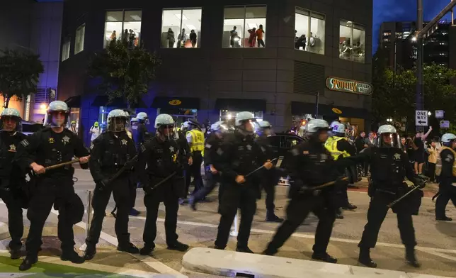 People watch from the second floor of a building as police block the street during a demonstration near the Israeli Consulate during the Democratic National Convention Tuesday, Aug. 20, 2024, in Chicago. (AP Photo/Julio Cortez)