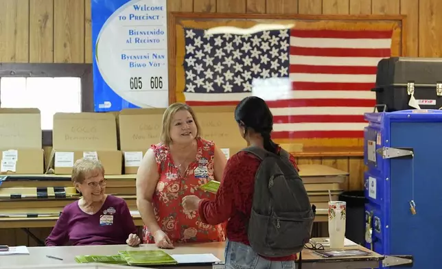 Poll worker Essie Palmer Yera, center, who as inspector is tasked with making sure voters receive the correct ballot for their precinct and party affiliation, hands a voter a ballot at a polling station inside the American Legion in South Miami, Fla., during voting in Florida's primary election, Tuesday, Aug. 20, 2024. (AP Photo/Rebecca Blackwell)