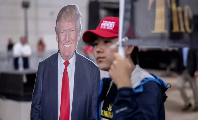 A supporter walks past a cardboard cutout of Republican presidential nominee former President Donald Trump before a campaign rally at the Mohegan Sun Arena at Casey Plaza in Wilkes-Barre, Pa., Saturday, Aug. 17, 2024. (AP Photo/Laurence Kesterson)