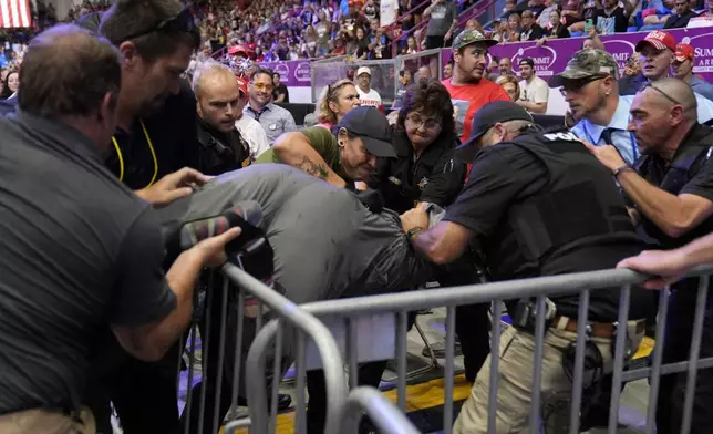 Police remove a man, center, who had climbed over barricades and onto the media riser, as Republican presidential nominee former President Donald Trump speaks at a campaign event, Friday, Aug. 30, 2024, in Johnstown, Pa. (AP Photo/Alex Brandon)