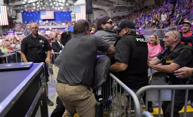 Police remove a man, center with sunglasses, who had climbed onto the media riser, as Republican presidential nominee former President Donald Trump speaks at a campaign event, Friday, Aug. 30, 2024, in Johnstown, Pa. (AP Photo/Alex Brandon)