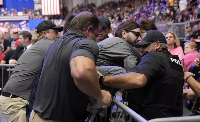 Police remove a man, center with sunglasses, who had climbed onto the media riser, as Republican presidential nominee former President Donald Trump speaks at a campaign event, Friday, Aug. 30, 2024, in Johnstown, Pa. (AP Photo/Alex Brandon)