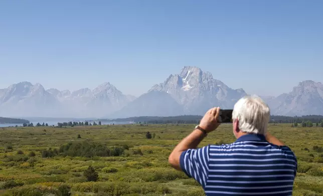 Steve Carringer of Tennessee takes a photo of the mountains at Jackson Lake Lodge, the site of the Jackson Hole Economic Symposium, in Grand Teton National Park near Moran, Wyo., on Thursday, Aug. 22, 2024. (AP Photo/Amber Baesler)