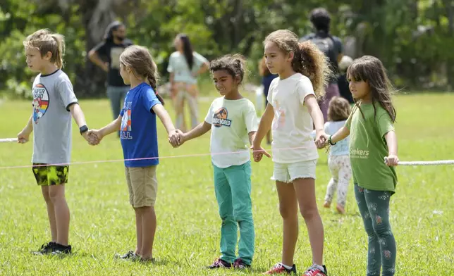 Children hold hands as they use yarn to outline the area a pickleball court would occupy, during a protest against Gov. Ron DeSantis' plan to develop state parks with business ventures such as golf courses, pickleball courts and large hotels, during a demonstration at Oleta River State Park, Tuesday, Aug. 27, 2024, in North Miami Beach, Fla. (AP Photo/Wilfredo Lee)