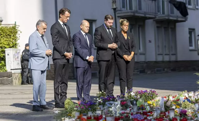 From left, Herbert Reul, Minister of the Interior of North Rhine-Westphalia, Hendrik Wüst, Minister President of North Rhine-Westphalia, German Chancellor Olaf Scholz, Tim Kurzbach, Mayor of Solingen, and Mona Neubaur, Deputy Minister President of North Rhine-Westphalia, pay their respects, in front of floral tributes left, near the scene of a knife attack, in Solingen, Germany, Monday, Aug. 26, 2024. (Thomas Banneyer/dpa via AP)