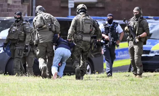 The alleged perpetrator of the knife attack in Solingen is escorted to a police car in Karlsruhe, Germany, Sunday, Aug. 25, 2024. German police say a 26-year-old man has turned himself in, saying he was responsible for the deadly Solingen knife attack that left three dead and eight wounded at a festival marking the city’s 650th anniversary. (Uli Deck/dpa via AP)