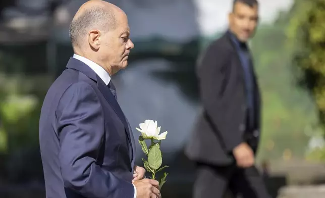 Germany Chancellor Olaf Scholz lays a flower at a church, near the scene of a knife attack, in Solingen, Germany, Monday, Aug. 26, 2024. (Thomas Banneyer/dpa via AP)