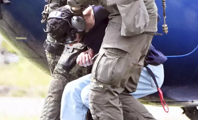 The alleged perpetrator of the knife attack in Solingen is escorted from a helicopter in Karlsruhe, Germany, Sunday, Aug. 25, 2024. German police say a 26-year-old man has turned himself in, saying he was responsible for the deadly Solingen knife attack that left three dead and eight wounded at a festival marking the city’s 650th anniversary. (Uli Deck/dpa via AP)