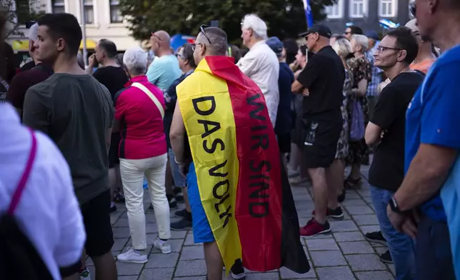 A man covering with a German national flag with the slogan "We are the people" listens to Bjoern Hoecke, top candidate of the far-right Alternative for Germany party, or AfD, during an election campaign rally of the party for upcoming state elections in Suhl, Germany, Tuesday, Aug. 13, 2024. (AP Photo/Markus Schreiber)