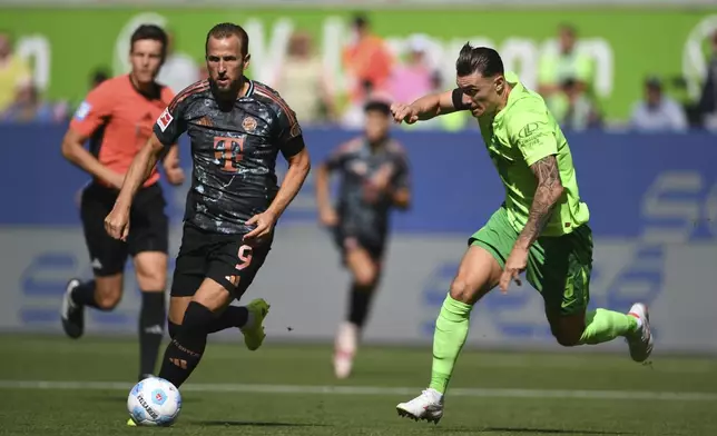 Bayern's Harry Kane, left, in action against Wolfsburg's Cedric Zesiger during the German Bundesliga soccer match between VfL Wolfsburg and FC Bayern Munich at the Volkswagen Arena in Wolfsburg, Germany, Sunday, Aug. 27, 2024. (Swen Pfoertner/dpa via AP)