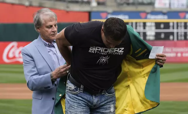 Former Oakland Athletics player Jose Canseco, right, is helped into his green jacket by Tony La Russa, left, after being inducted into the team's Hall of Fame before a baseball game against the San Francisco Giants, Saturday, Aug. 17, 2024, in Oakland, Calif. (AP Photo/Godofredo A. Vásquez)