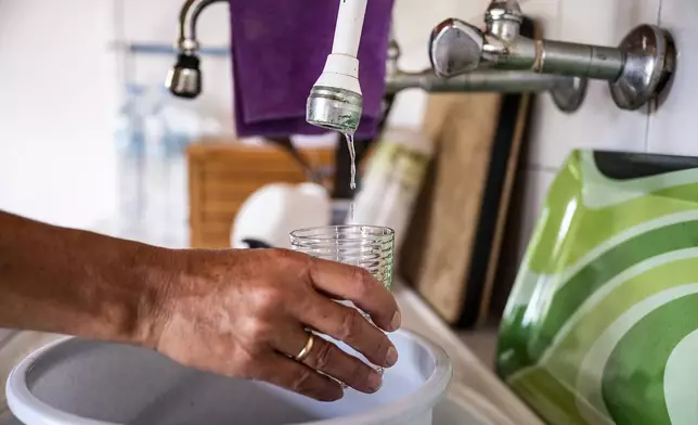 Haroula Psaropoulou, tries to fill a glass with water that drip from a faucet, in the village of Nea Potidea, at Halkidiki peninsula, northern Greece, Aug. 19, 2024. A severe drought in northern Greece, worsened by successive heatwaves and low rainfall, is causing water shortages that are threatening agriculture, drying up lakes, and stressing local communities dependent on tourism. (AP Photo/Giannis Papanikos)