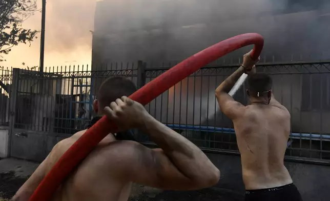 Two men try to extinguish the flames at a burning business during a fire in northern Athens, Monday, Aug. 12, 2024, as hundreds of firefighters tackle a major wildfire raging out of control on fringes of Greek capital. (AP Photo/Michael Varaklas)