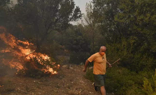 A man passes next to flames during a fire in northern Athens, Monday, Aug. 12, 2024, as hundreds of firefighters tackle a major wildfire raging out of control on fringes of Greek capital. (AP Photo/Michael Varaklas)