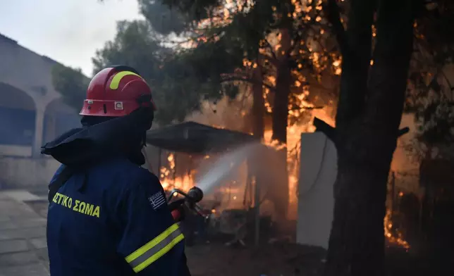 A firefighter works to extinguish the flames at a burning house in northern Athens, Monday, Aug. 12, 2024, as hundreds of firefighters tackle a major wildfire raging out of control on fringes of Greek capital. (AP Photo/Michael Varaklas)