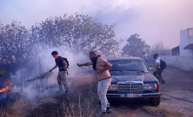 Volunteers try to extinguish the flames near a house during a fire in northern Athens, Monday, Aug. 12, 2024, as hundreds of firefighters tackle a major wildfire raging out of control on fringes of Greek capital. (AP Photo/Aggelos Barai)