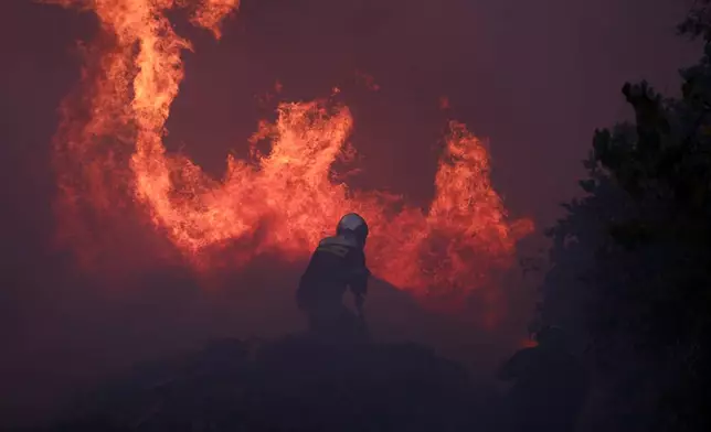 A firefighter tries to extinguish the flames at a business during a fire in northern Athens, Monday, Aug. 12, 2024, as hundreds of firefighters tackle a major wildfire raging out of control on fringes of Greek capital. (AP Photo/Aggelos Barai)