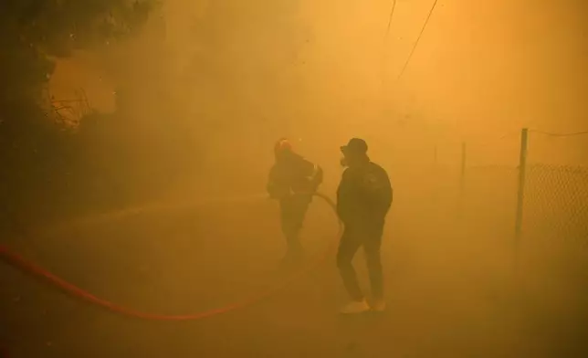 A firefighter and volunteer try to extinguish a fire in northern Athens, Monday, Aug. 12, 2024, as hundreds of firefighters tackle a major wildfire raging out of control on fringes of Greek capital. (AP Photo/Michael Varaklas)