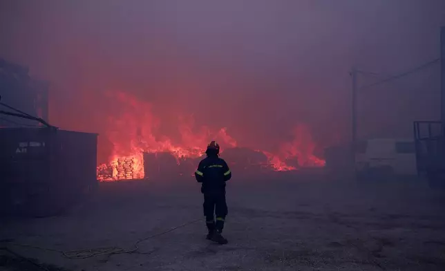 A firefighter stands in front of a burning business during a fire in northern Athens, Monday, Aug. 12, 2024, as hundreds of firefighters tackle a major wildfire raging out of control on fringes of Greek capital. (AP Photo/Aggelos Barai)