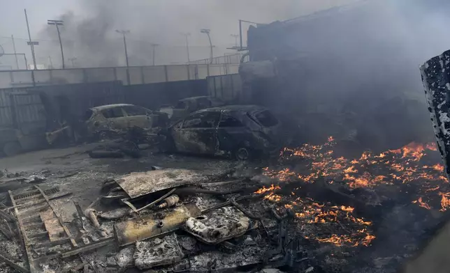 Flames burn next to damaged cars at a business during a fire in northern Athens, Monday, Aug. 12, 2024, as hundreds of firefighters tackle a major wildfire raging out of control on fringes of Greek capital. (AP Photo/Michael Varaklas)