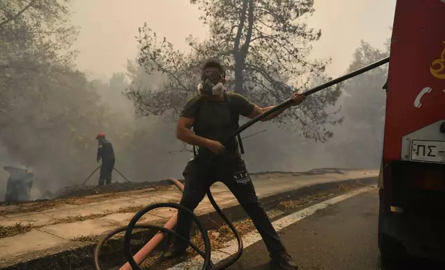 A firefighter and volunteer try to extinguish a fire in northern Athens, Monday, Aug. 12, 2024, as hundreds of firefighters tackle a major wildfire raging out of control on fringes of Greek capital. (AP Photo/Michael Varaklas)