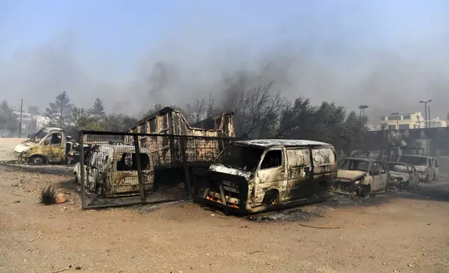 Flames burn a vehicle at a business during a fire in northern Athens, Monday, Aug. 12, 2024, as hundreds of firefighters tackle a major wildfire raging out of control on fringes of Greek capital. (AP Photo/Michael Varaklas)