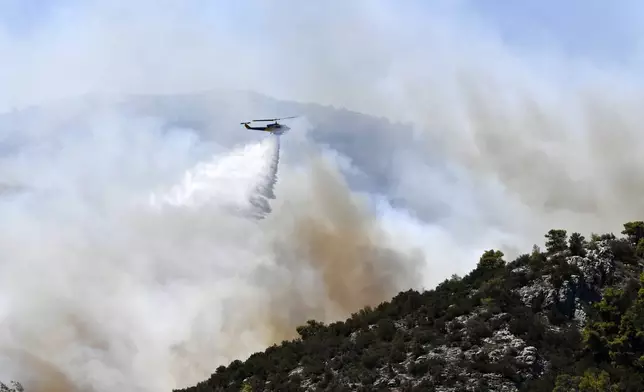 A helicopter drops water over a fire in Nea Makri, east of Athens, Monday, Aug. 12, 2024, as hundreds of firefighters tackle a major wildfire raging out of control on fringes of Greek capital. (AP Photo/Michael Varaklas)