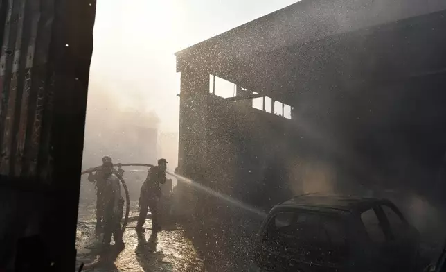 Two men and a volunteer firefighter try to extinguish the flames at a burning business during a fire in northern Athens, Monday, Aug. 12, 2024, as hundreds of firefighters tackle a major wildfire raging out of control on fringes of Greek capital. (AP Photo/Michael Varaklas)