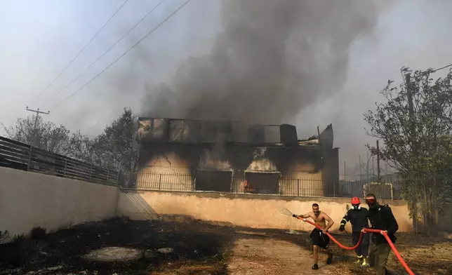 Two men and a volunteer firefighter try to extinguish the flames at a burning business during a fire in northern Athens, Monday, Aug. 12, 2024, as hundreds of firefighters tackle a major wildfire raging out of control on fringes of Greek capital. (AP Photo/Michael Varaklas)