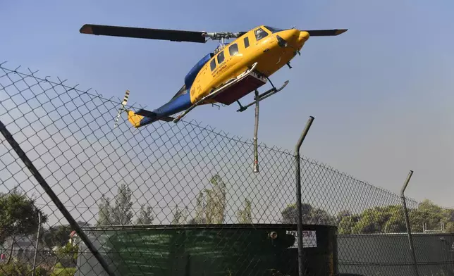 A helicopter approaches a water tank near Penteli, North-East of Athens, Greece, Monday, Aug. 12, 2024. Hundreds of firefighters backed by dozens of water-dropping planes and helicopters were battling the flames from first light Monday. (AP Photo/Michael Varaklas