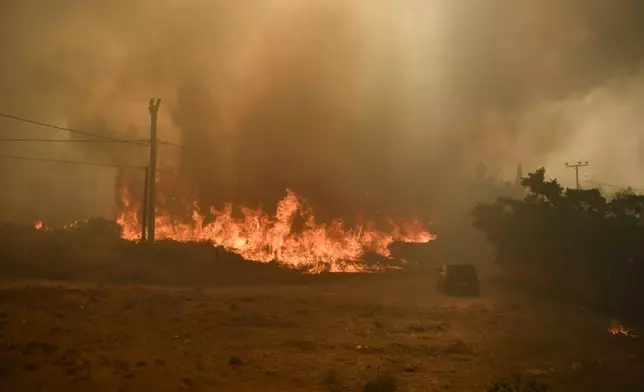 A car is seen near flames in Dioni, northeast of Athens, Greece, Monday, Aug. 12, 2024. Hundreds of firefighters backed by dozens of water-dropping planes and helicopters were battling the flames from first light Monday, with a major forest fire that began the previous day raging out of control on the fringes of Athens, fanned by strong winds. (AP Photo/Michael Varaklas)