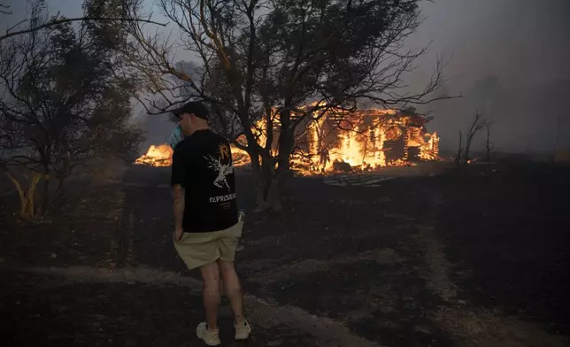 A man reacts as a house is on fire in Varnava village during a wildfire, north of Athens, Greece, Sunday, Aug. 11, 2024, with many regions of the country on high alert due to high temperatures and wind speeds. (AP Photo/Michael Varaklas)