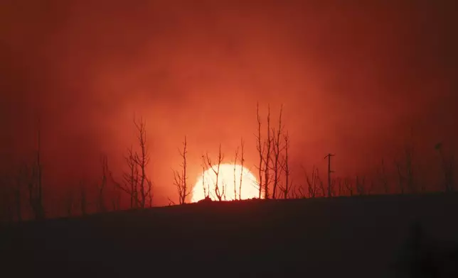 The sun sets behinds burned trees in Varnava village during a wildfire, north of Athens, Greece, Sunday, Aug. 11, 2024, with many regions of the country on high alert due to high temperatures and wind speeds. (AP Photo/Michael Varaklas)