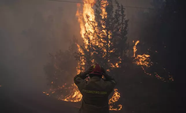 A firefighter adjusts his helmet in Varnava village during a wildfire, north of Athens, Greece, Sunday, Aug. 11, 2024, with many regions of the country on high alert due to high temperatures and wind speeds. (AP Photo/Michael Varaklas)