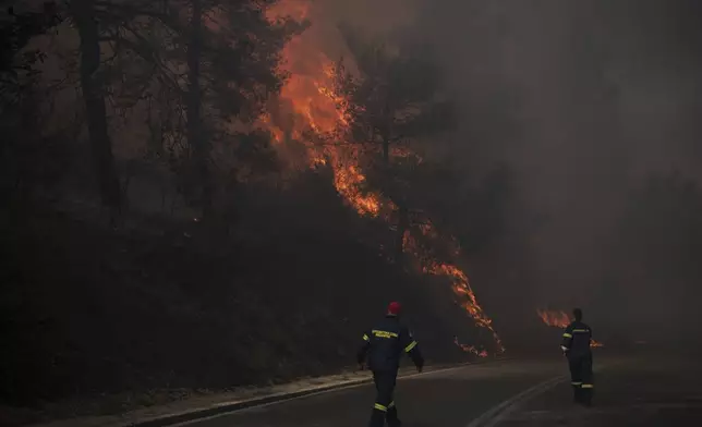 Firefighters inspect flames near a road in Varnava village during a wildfire, north of Athens, Greece, Sunday, Aug. 11, 2024, with many regions of the country on high alert due to high temperatures and wind speeds. (AP Photo/Michael Varaklas)